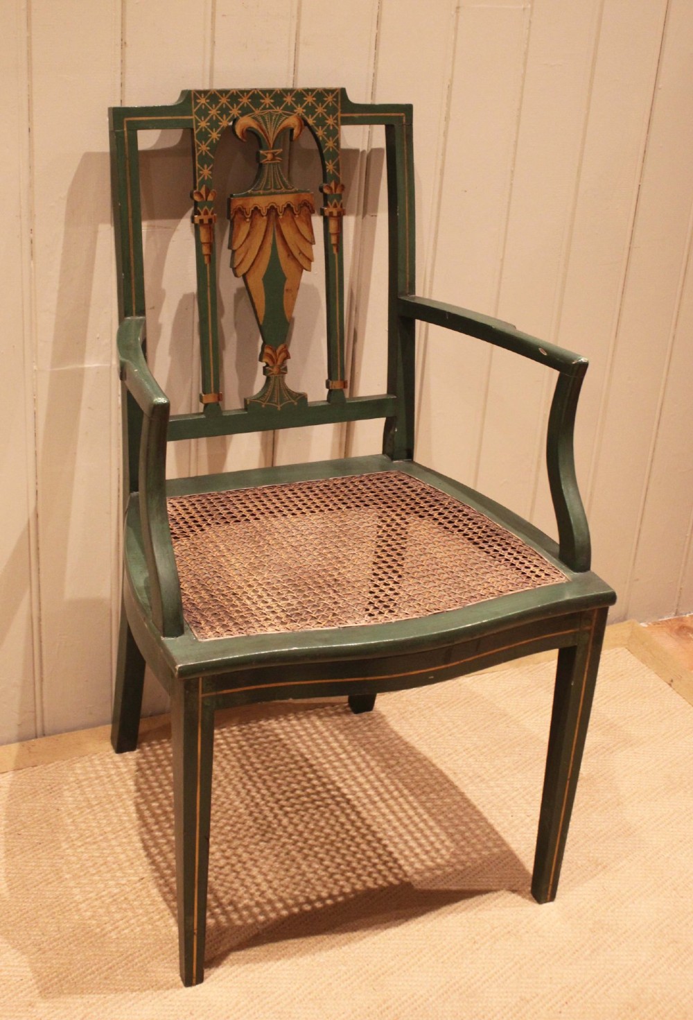 A dark green painted Hepplewhite style armchair featuring a woven cane seat, curved armrests, and hand-painted neoclassical motifs on the backrest. View II