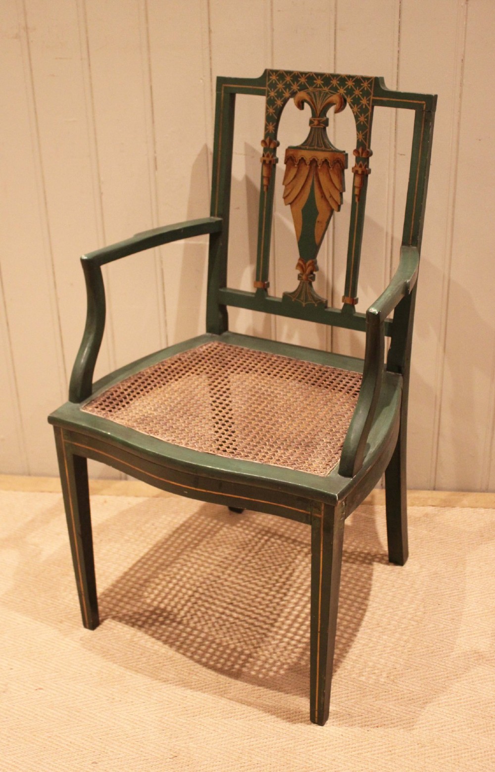 A dark green painted Hepplewhite style armchair featuring a woven cane seat, curved armrests, and hand-painted neoclassical motifs on the backrest. View III