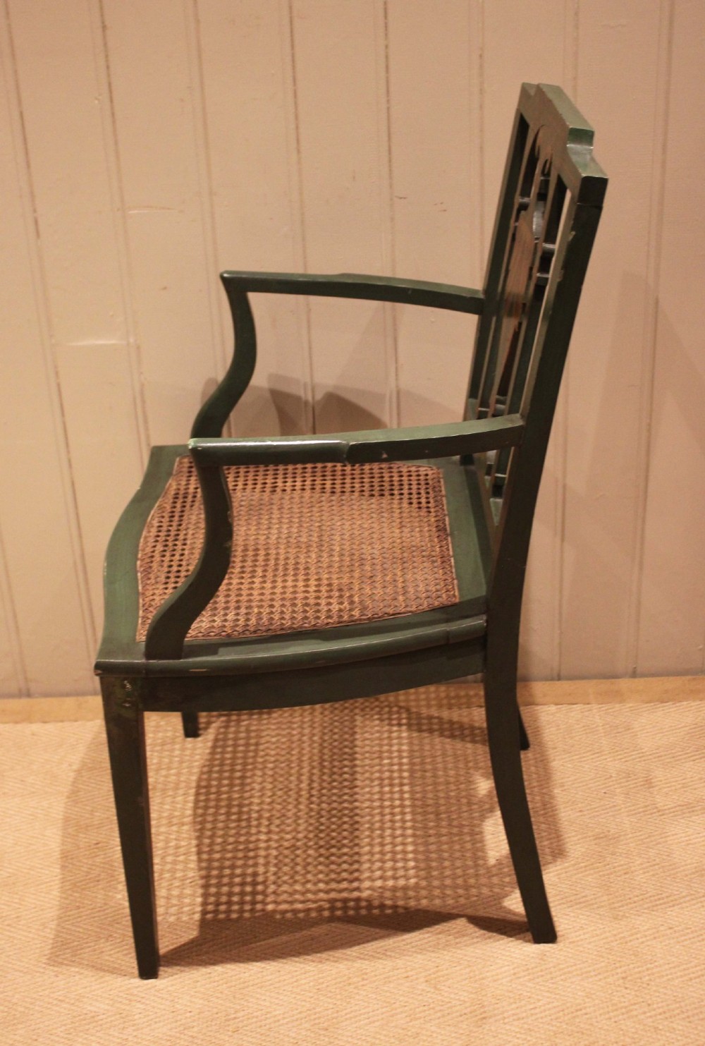 A dark green painted Hepplewhite style armchair featuring a woven cane seat, curved armrests, and hand-painted neoclassical motifs on the backrest. View V
