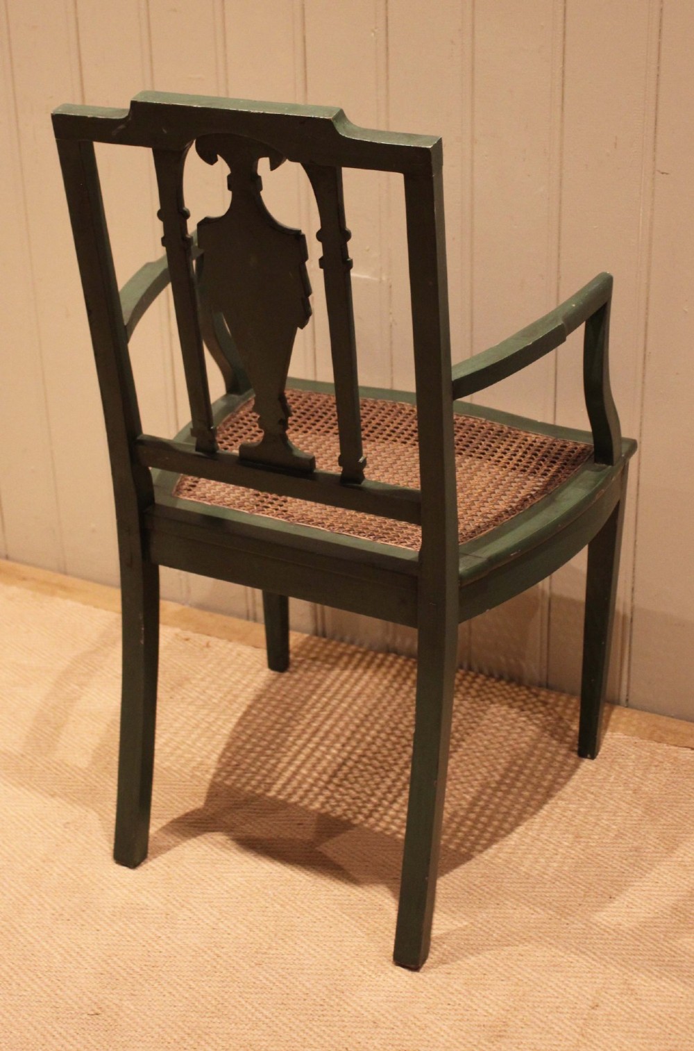 A dark green painted Hepplewhite style armchair featuring a woven cane seat, curved armrests, and hand-painted neoclassical motifs on the backrest. View VII