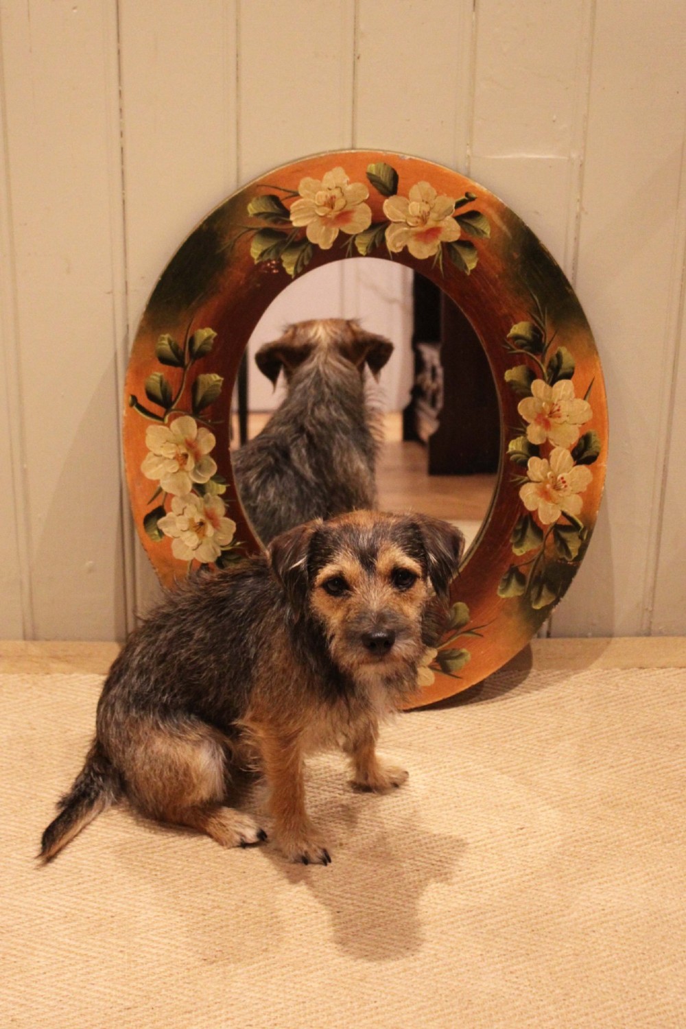 An oval wooden wall mirror featuring hand-painted cream floral blossoms and green foliage on an amber-toned frame. View X