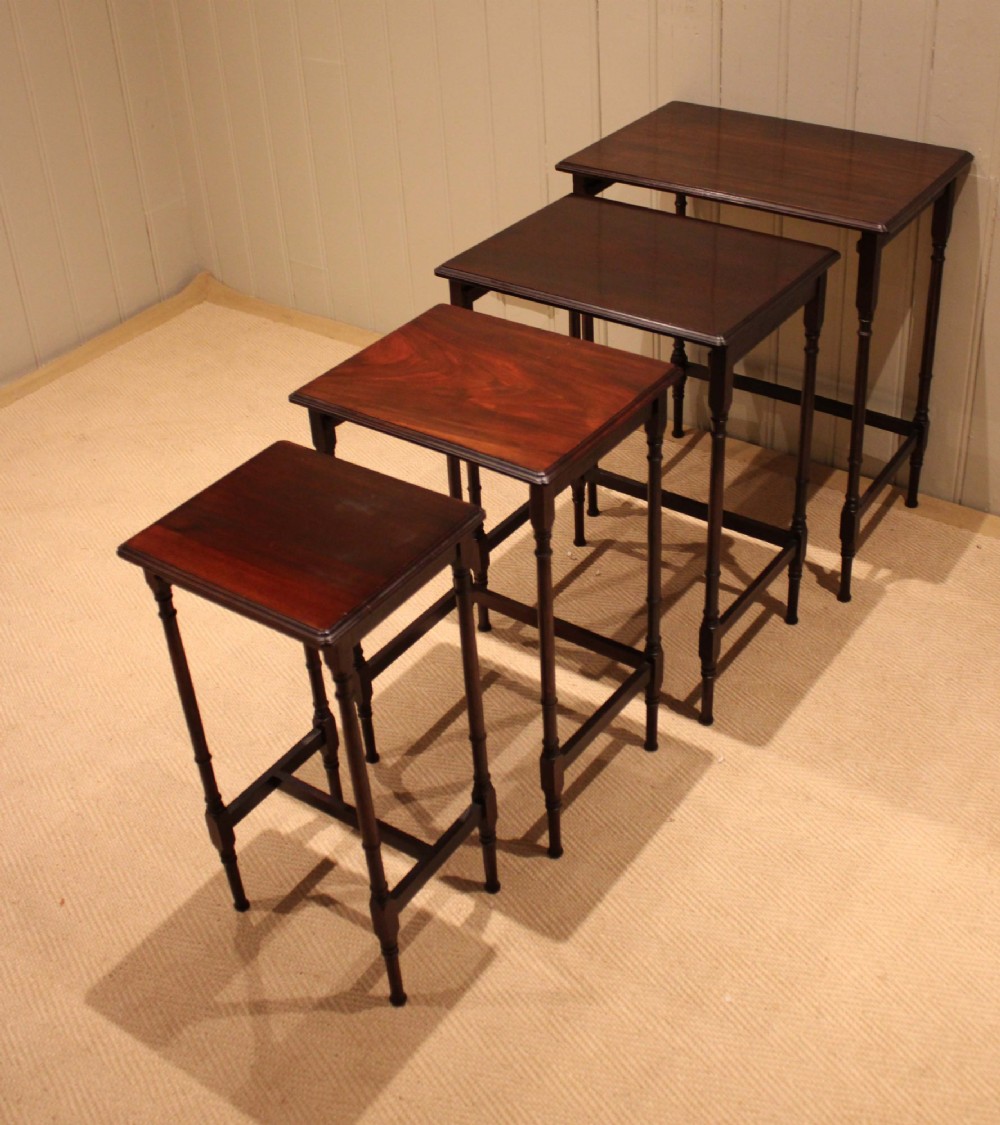 A set of four graduated mahogany nesting tables featuring rectangular tops with moulded edges, slender turned legs, and connecting stretchers. View IV
