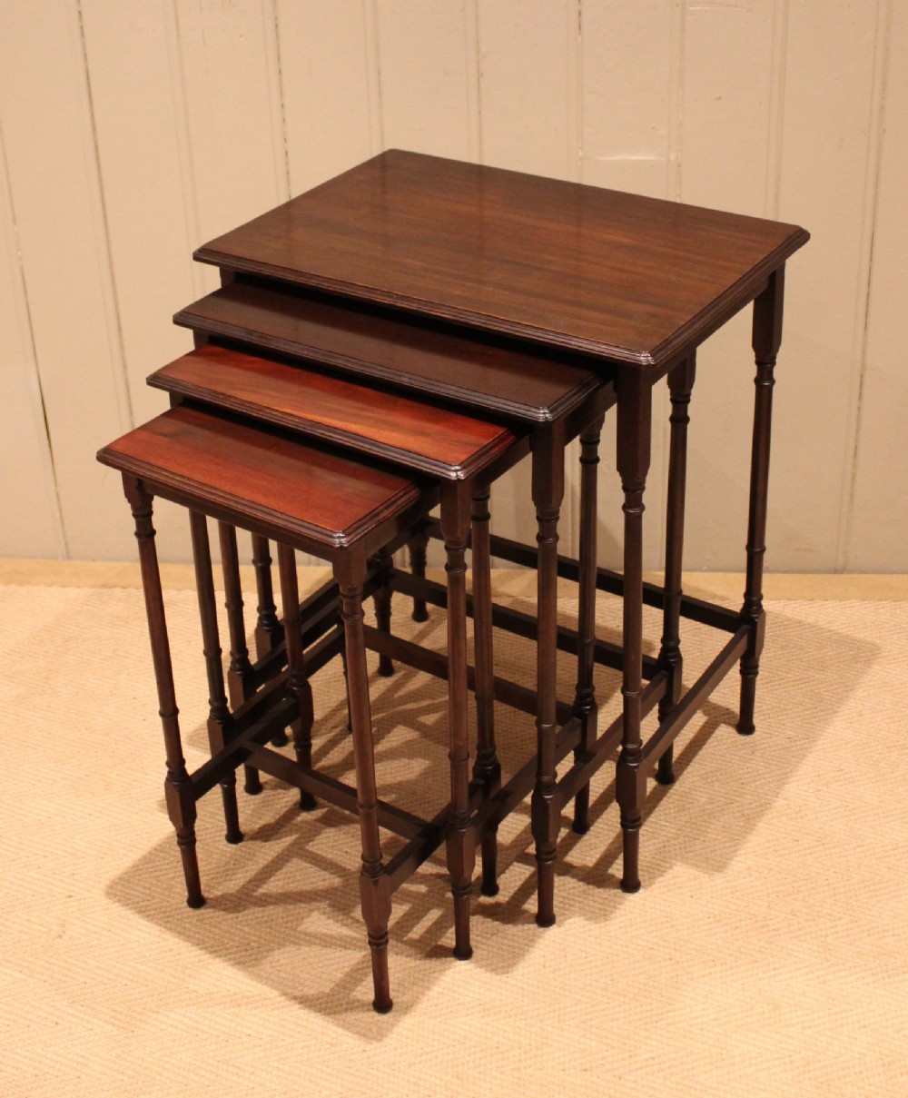 A set of four graduated mahogany nesting tables featuring rectangular tops with moulded edges, slender turned legs, and connecting stretchers. View X