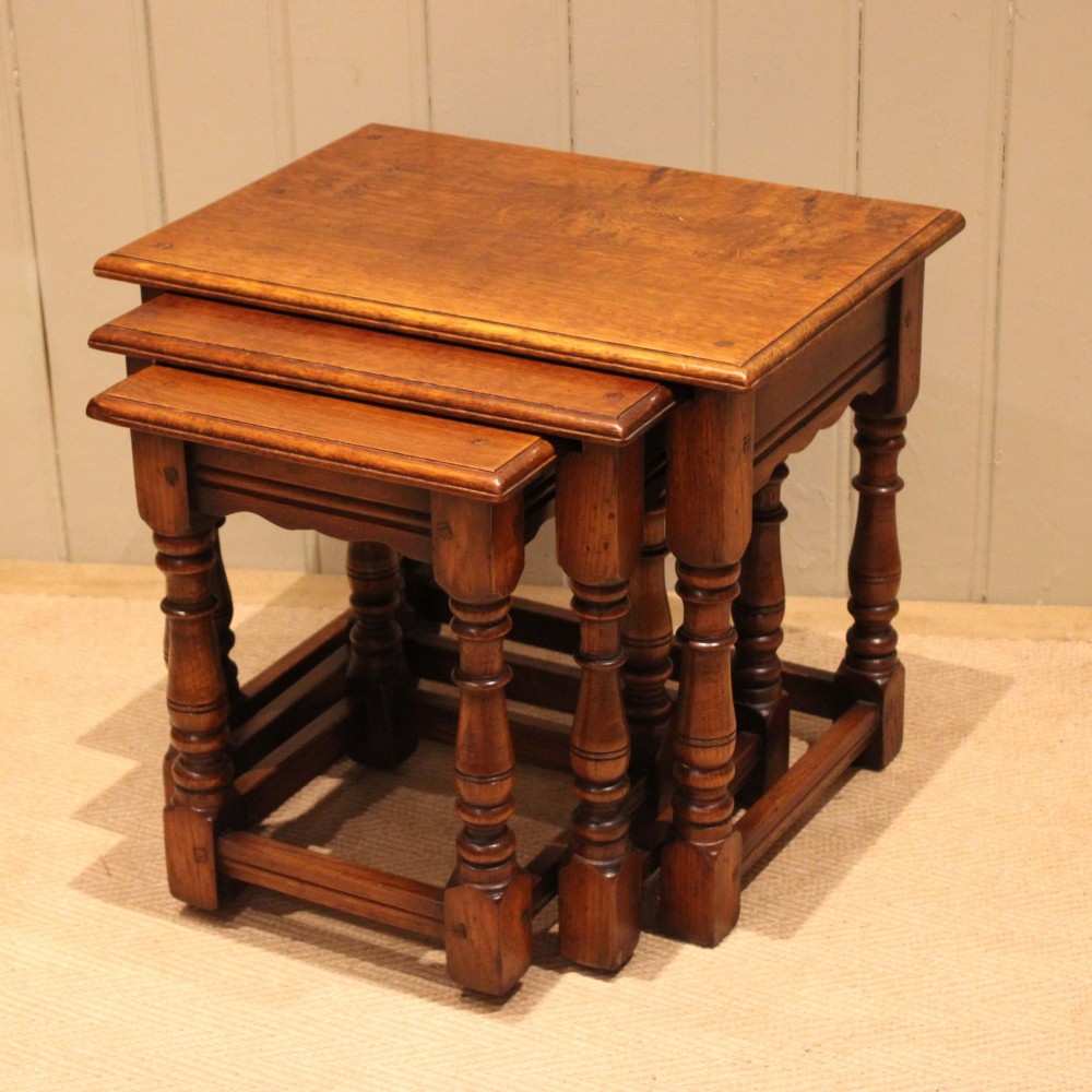 A set of three graduating solid oak nesting tables featuring turned legs, box stretchers, and rectangular molded tops.