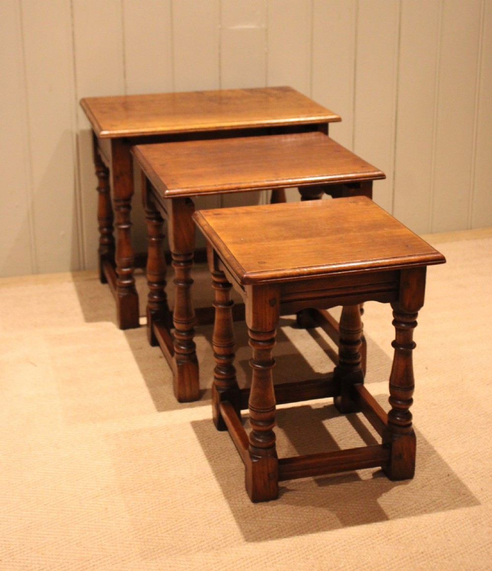 A set of three graduating solid oak nesting tables featuring turned legs, box stretchers, and rectangular molded tops. View II