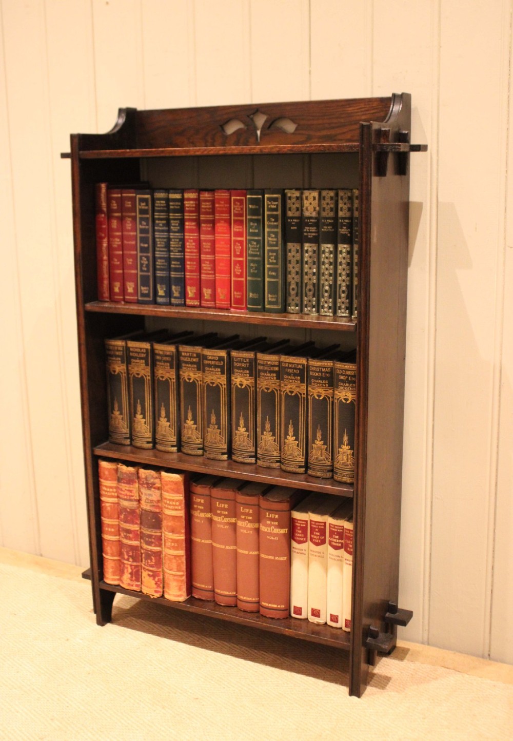 A dark oak open bookcase featuring three shelves, protruding pegged side joints, and a shaped top gallery with a pierced motif.