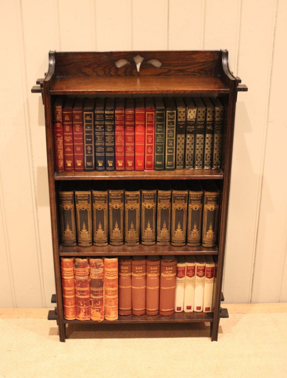 A dark oak open bookcase featuring three shelves, protruding pegged side joints, and a shaped top gallery with a pierced motif. View III