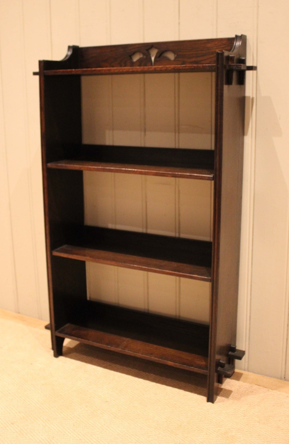 A dark oak open bookcase featuring three shelves, protruding pegged side joints, and a shaped top gallery with a pierced motif. View IV