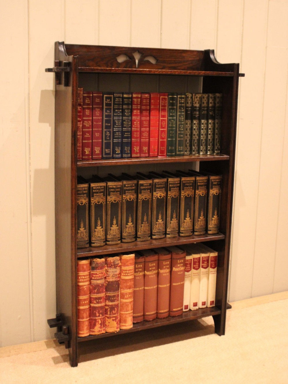 A dark oak open bookcase featuring three shelves, protruding pegged side joints, and a shaped top gallery with a pierced motif. View V