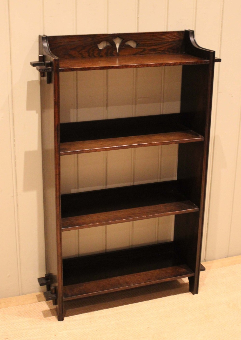 A dark oak open bookcase featuring three shelves, protruding pegged side joints, and a shaped top gallery with a pierced motif. View VI