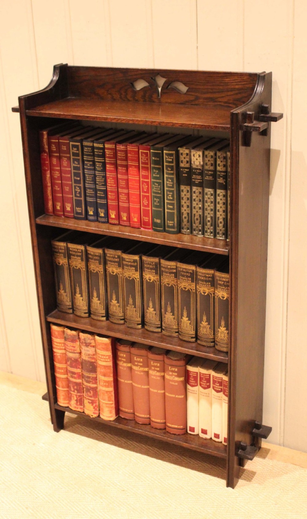 A dark oak open bookcase featuring three shelves, protruding pegged side joints, and a shaped top gallery with a pierced motif. View VII