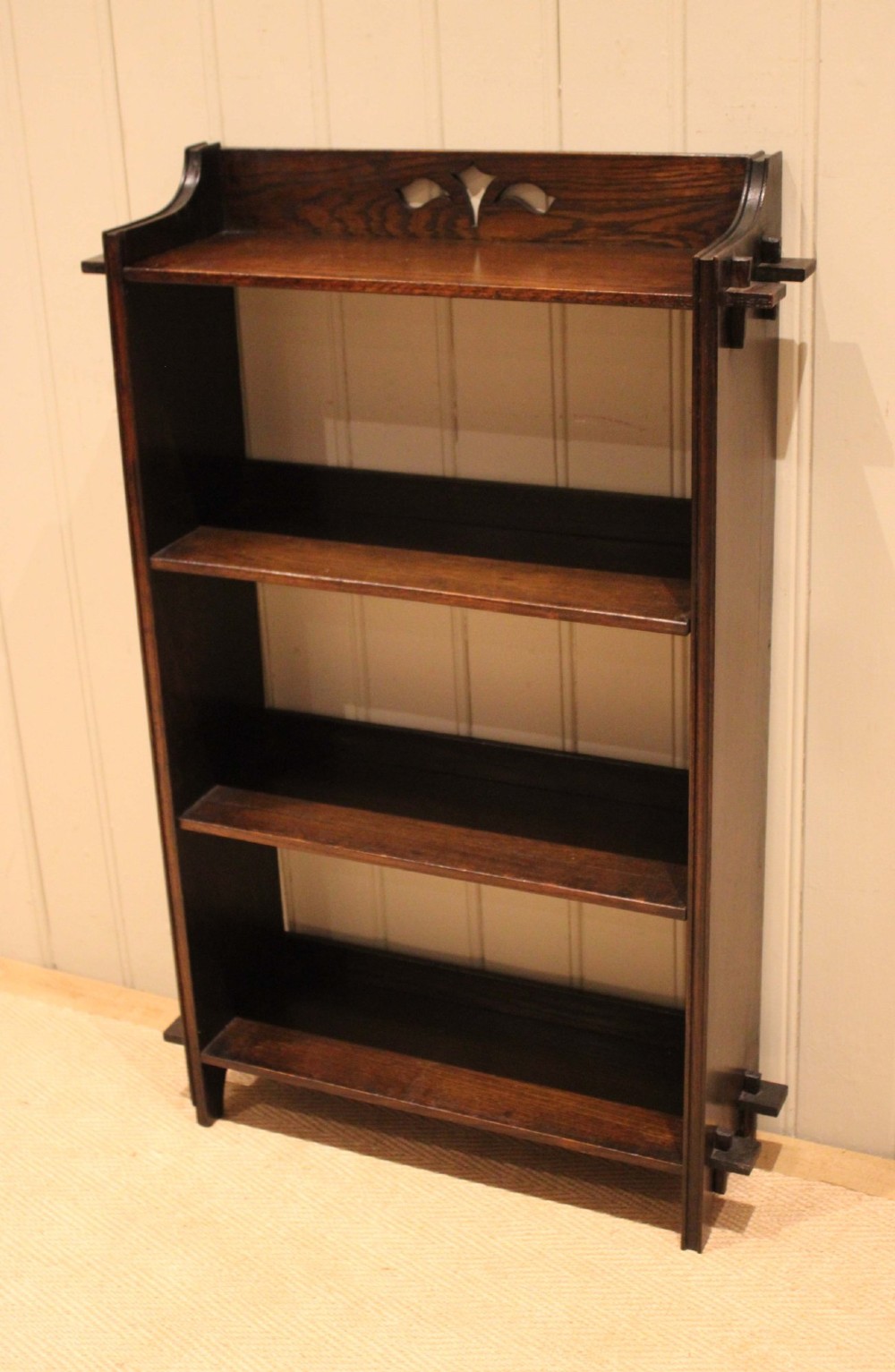 A dark oak open bookcase featuring three shelves, protruding pegged side joints, and a shaped top gallery with a pierced motif. View VIII