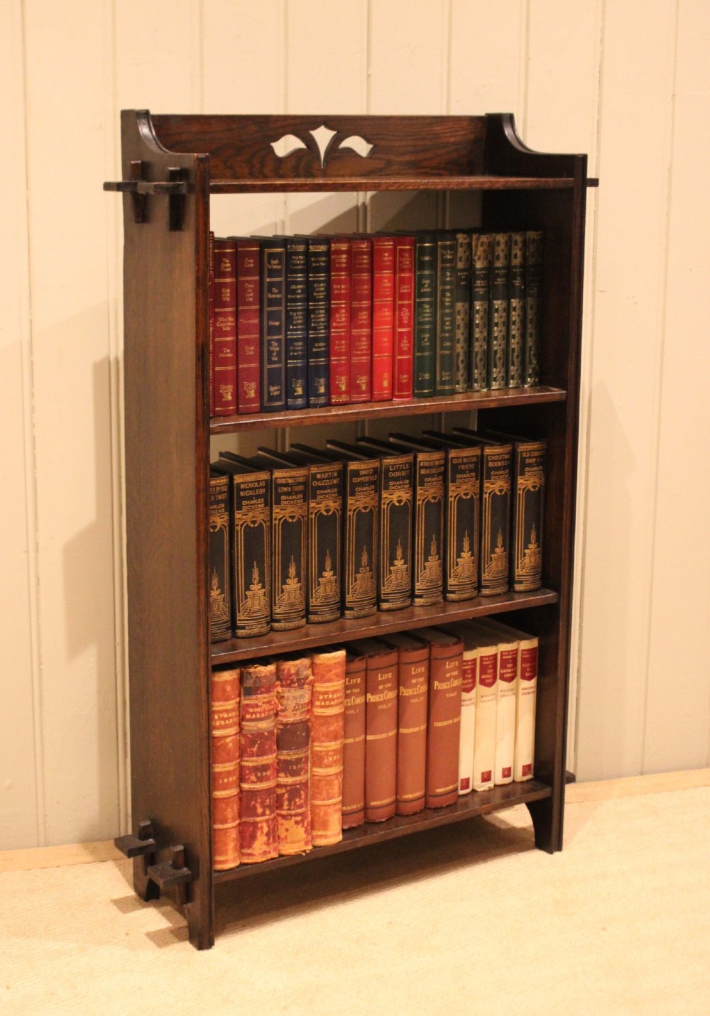 A dark oak open bookcase featuring three shelves, protruding pegged side joints, and a shaped top gallery with a pierced motif. View IX