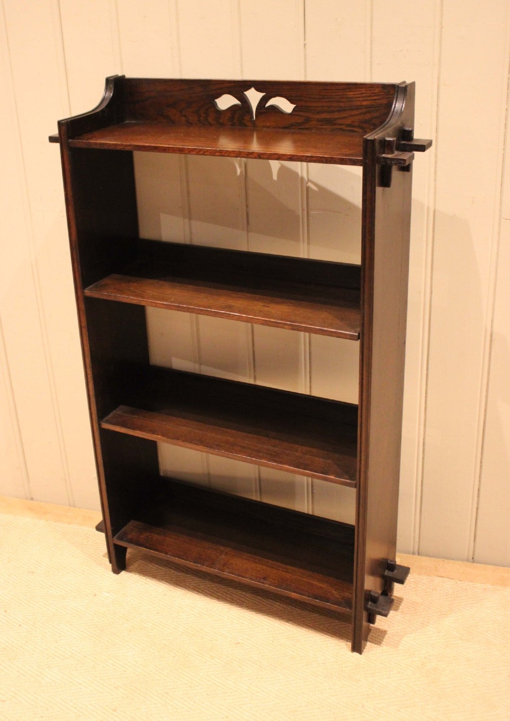 A dark oak open bookcase featuring three shelves, protruding pegged side joints, and a shaped top gallery with a pierced motif. View X