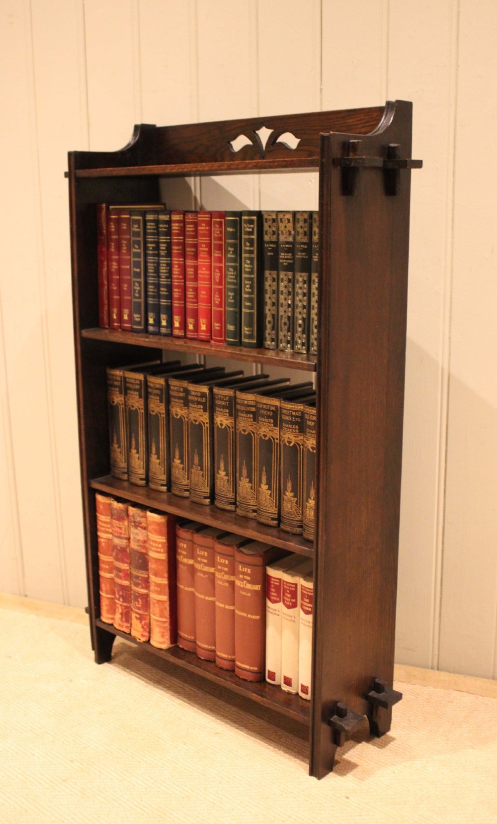 A dark oak open bookcase featuring three shelves, protruding pegged side joints, and a shaped top gallery with a pierced motif. View XI