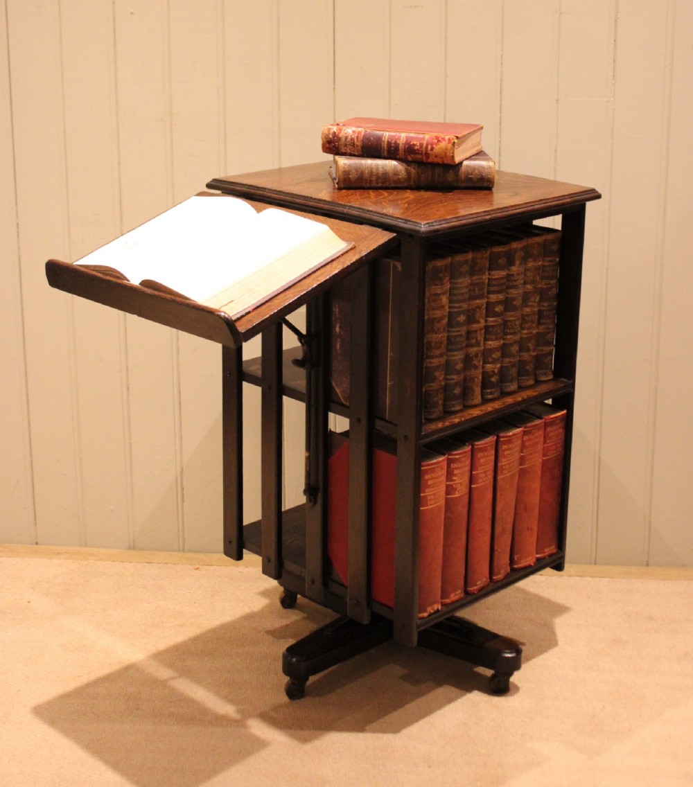A dark oak revolving bookcase featuring vertical slatted sides, an adjustable reading lectern, and a four-point base on castors.