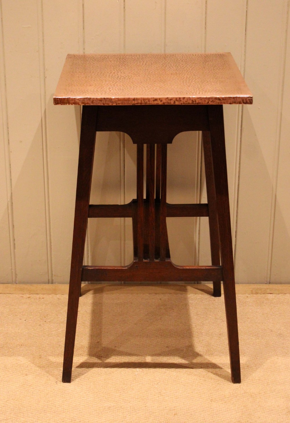 A square Arts and Crafts side table made of dark oak with a hand-hammered copper top, tapered legs, vertical slats, and cross stretchers.