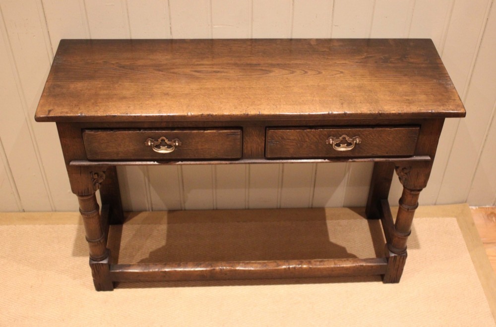 A solid oak server table featuring a rectangular top, two drawers with brass swan-neck handles, turned front legs, and a lower stretcher base. View II