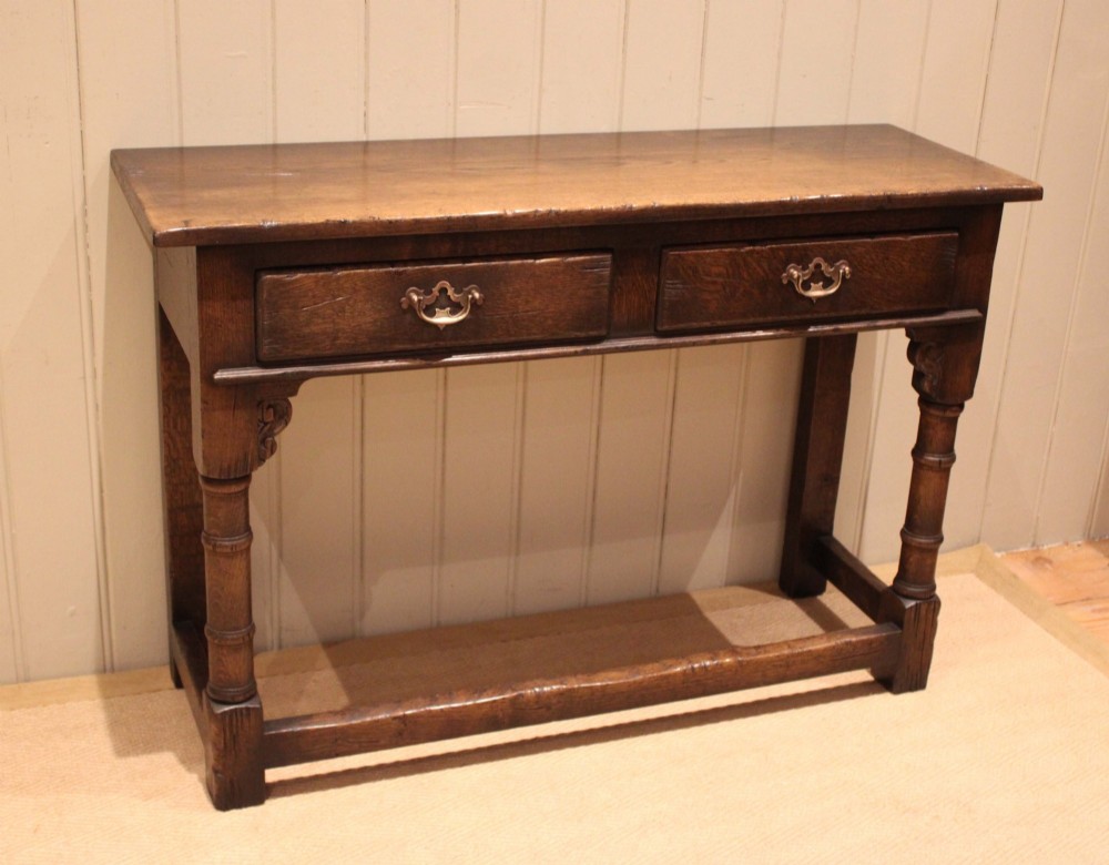 A solid oak server table featuring a rectangular top, two drawers with brass swan-neck handles, turned front legs, and a lower stretcher base. View III