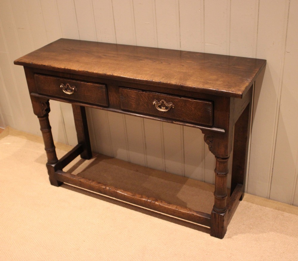 A solid oak server table featuring a rectangular top, two drawers with brass swan-neck handles, turned front legs, and a lower stretcher base. View IV