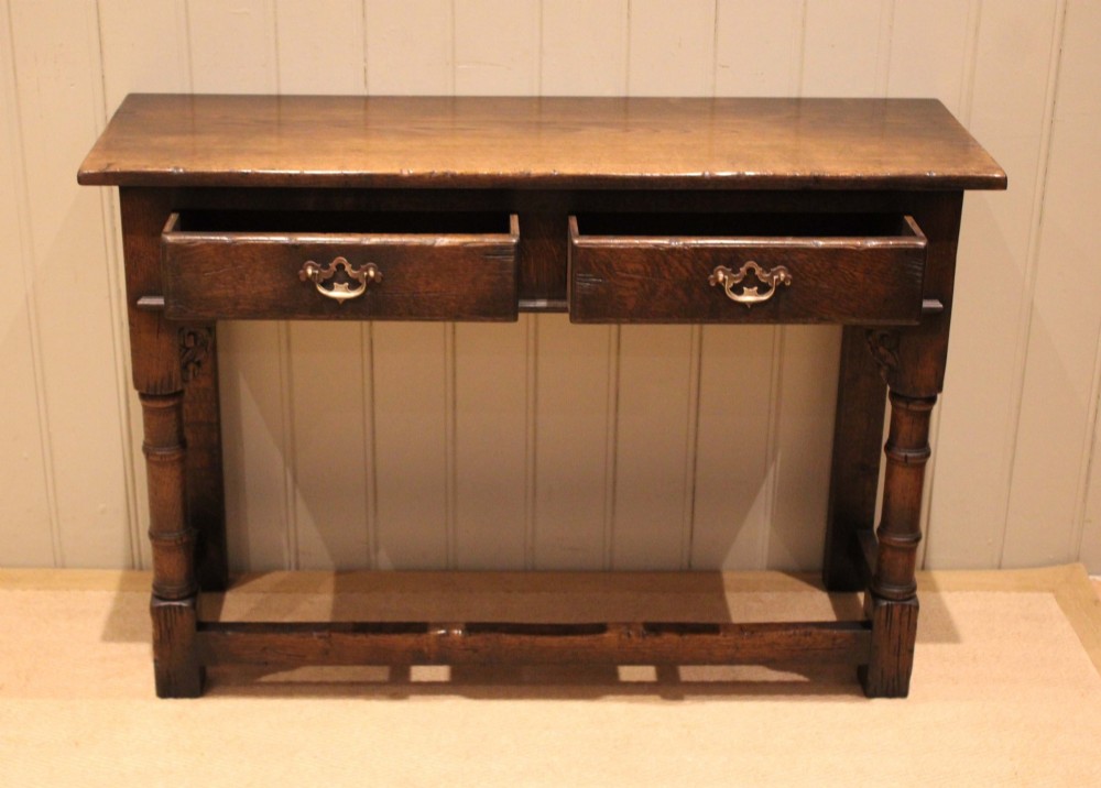 A solid oak server table featuring a rectangular top, two drawers with brass swan-neck handles, turned front legs, and a lower stretcher base. View V