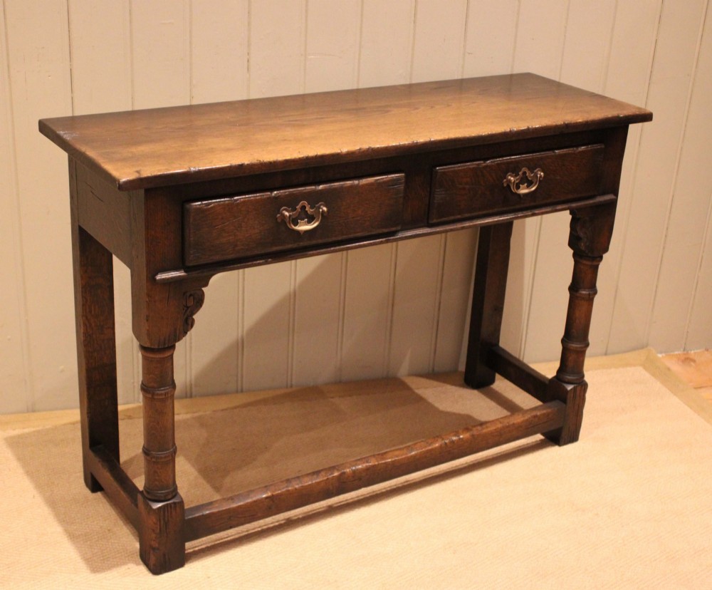 A solid oak server table featuring a rectangular top, two drawers with brass swan-neck handles, turned front legs, and a lower stretcher base. View VII