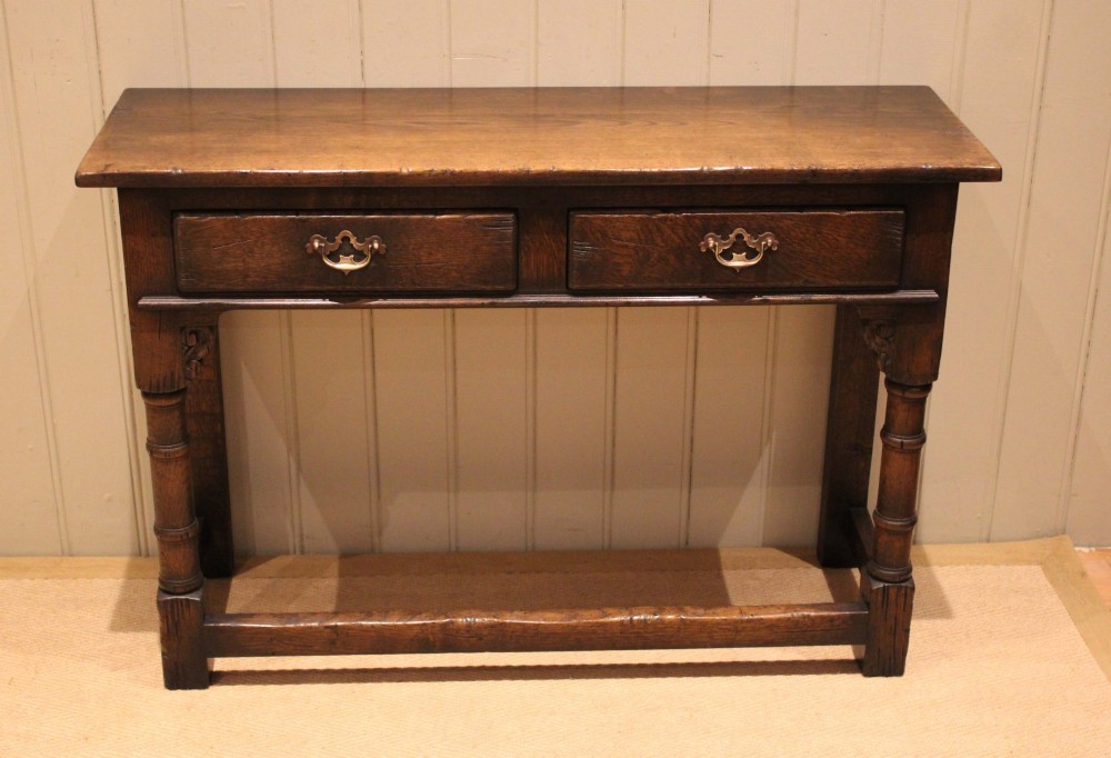 A solid oak server table featuring a rectangular top, two drawers with brass swan-neck handles, turned front legs, and a lower stretcher base. View X