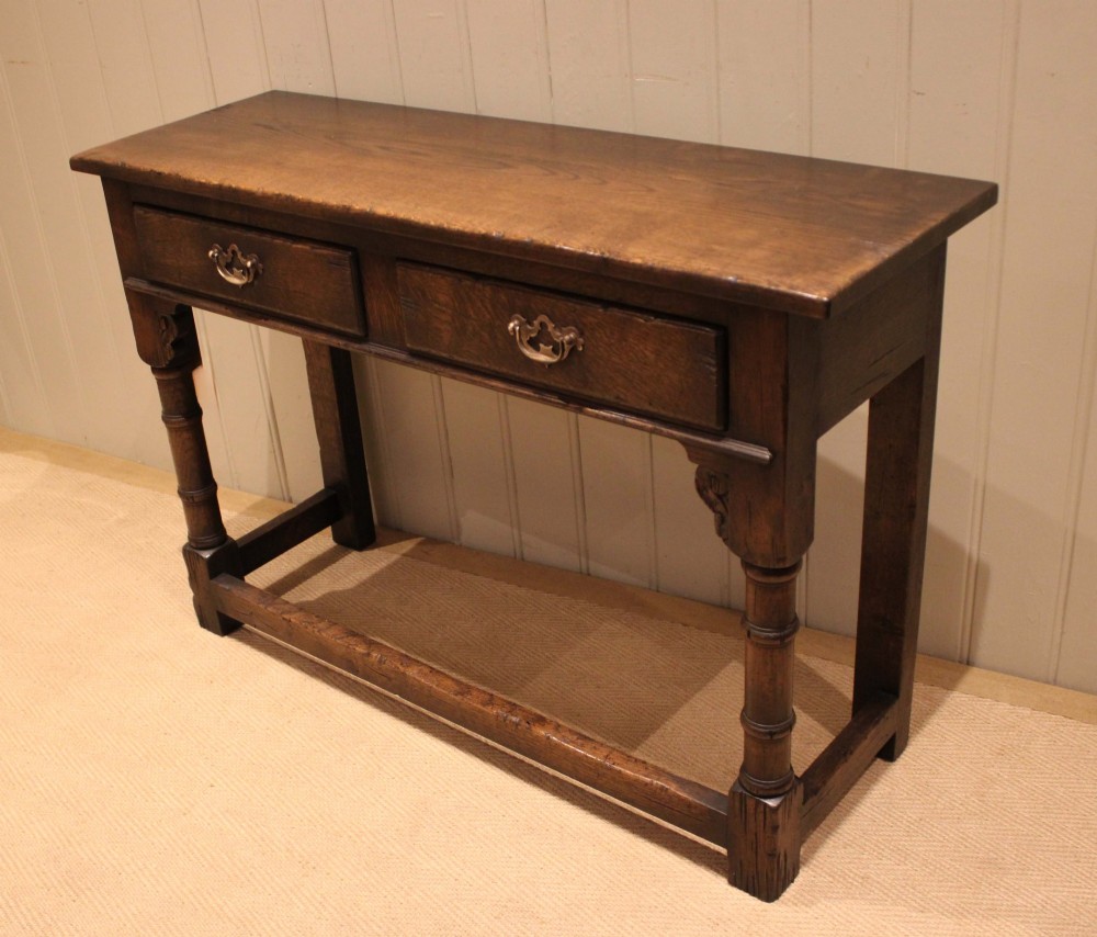 A solid oak server table featuring a rectangular top, two drawers with brass swan-neck handles, turned front legs, and a lower stretcher base. View XII