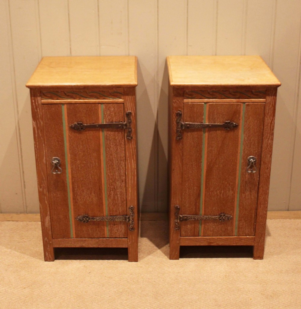 A pair of limed oak bedside cabinets featuring panelled single doors, wrought iron strap hinges, and subtle green painted accents.