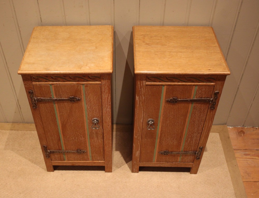 A pair of limed oak bedside cabinets featuring panelled single doors, wrought iron strap hinges, and subtle green painted accents. View IX