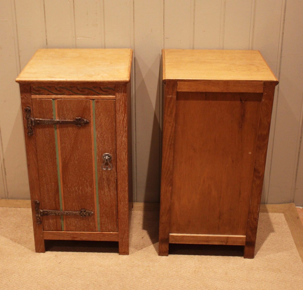 A pair of limed oak bedside cabinets featuring panelled single doors, wrought iron strap hinges, and subtle green painted accents. View X