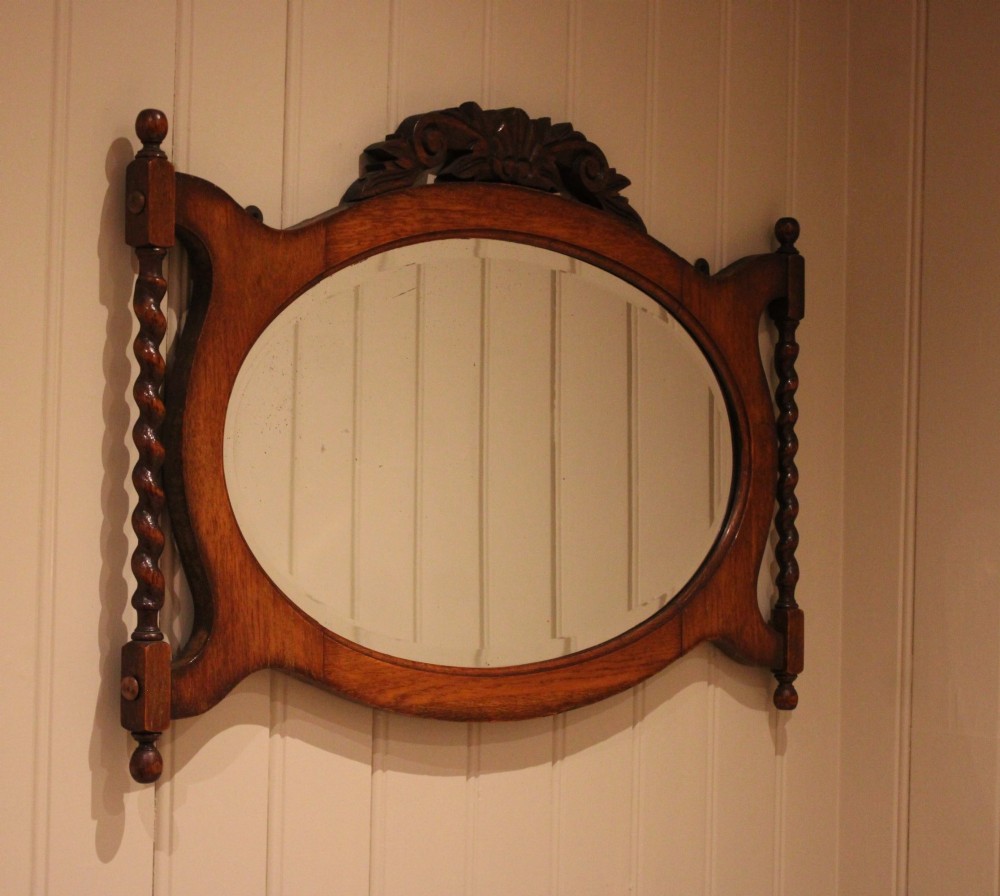 An oval glass wall mirror set within a dark carved oak frame featuring turned barley twist side pilasters and an ornate cresting. View III