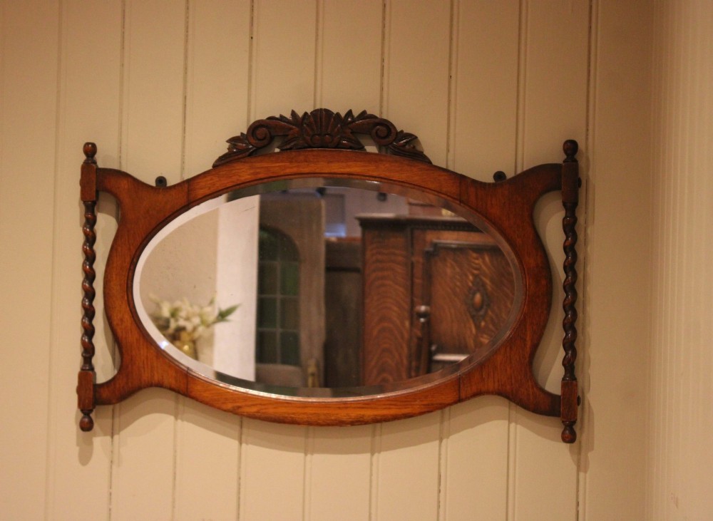 An oval glass wall mirror set within a dark carved oak frame featuring turned barley twist side pilasters and an ornate cresting. View IV