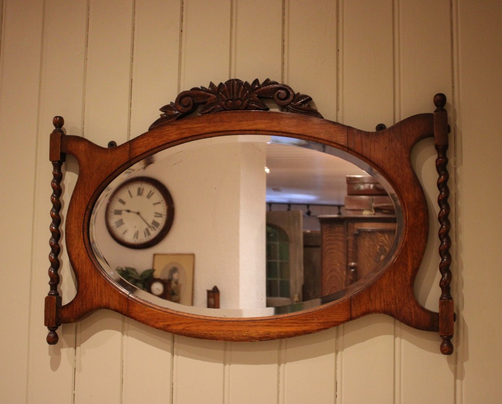 An oval glass wall mirror set within a dark carved oak frame featuring turned barley twist side pilasters and an ornate cresting. View VI
