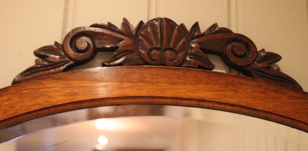 An oval glass wall mirror set within a dark carved oak frame featuring turned barley twist side pilasters and an ornate cresting. View VII