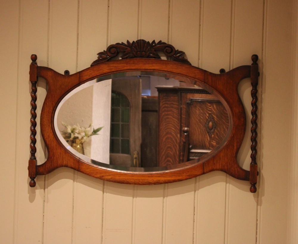 An oval glass wall mirror set within a dark carved oak frame featuring turned barley twist side pilasters and an ornate cresting. View VIII