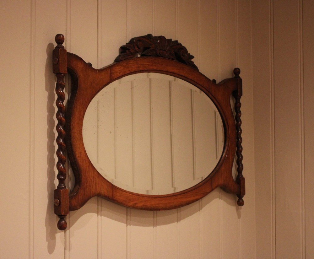 An oval glass wall mirror set within a dark carved oak frame featuring turned barley twist side pilasters and an ornate cresting. View IX