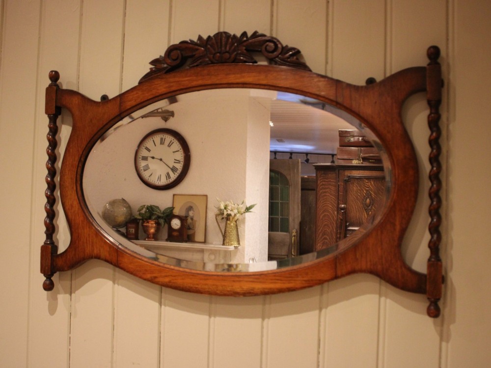 An oval glass wall mirror set within a dark carved oak frame featuring turned barley twist side pilasters and an ornate cresting. View X