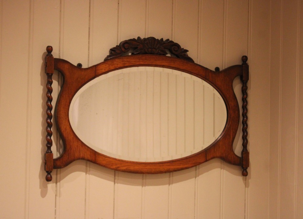 An oval glass wall mirror set within a dark carved oak frame featuring turned barley twist side pilasters and an ornate cresting. View XI