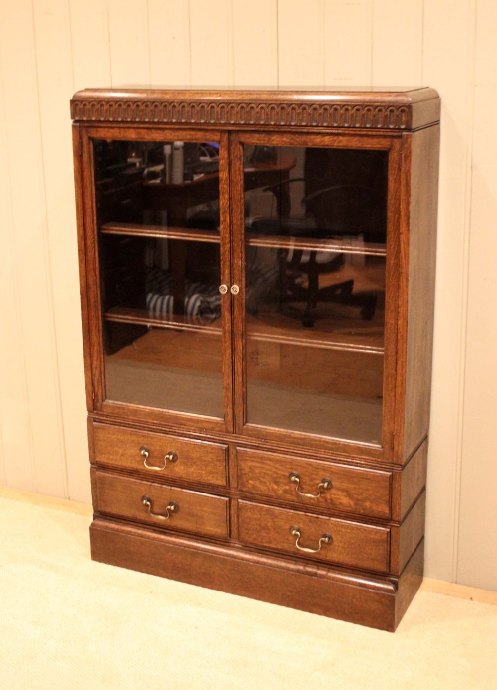 A medium brown oak glazed bookcase with two glass upper doors, carved egg-and-dart top moulding, and four drawers with brass handles. View II