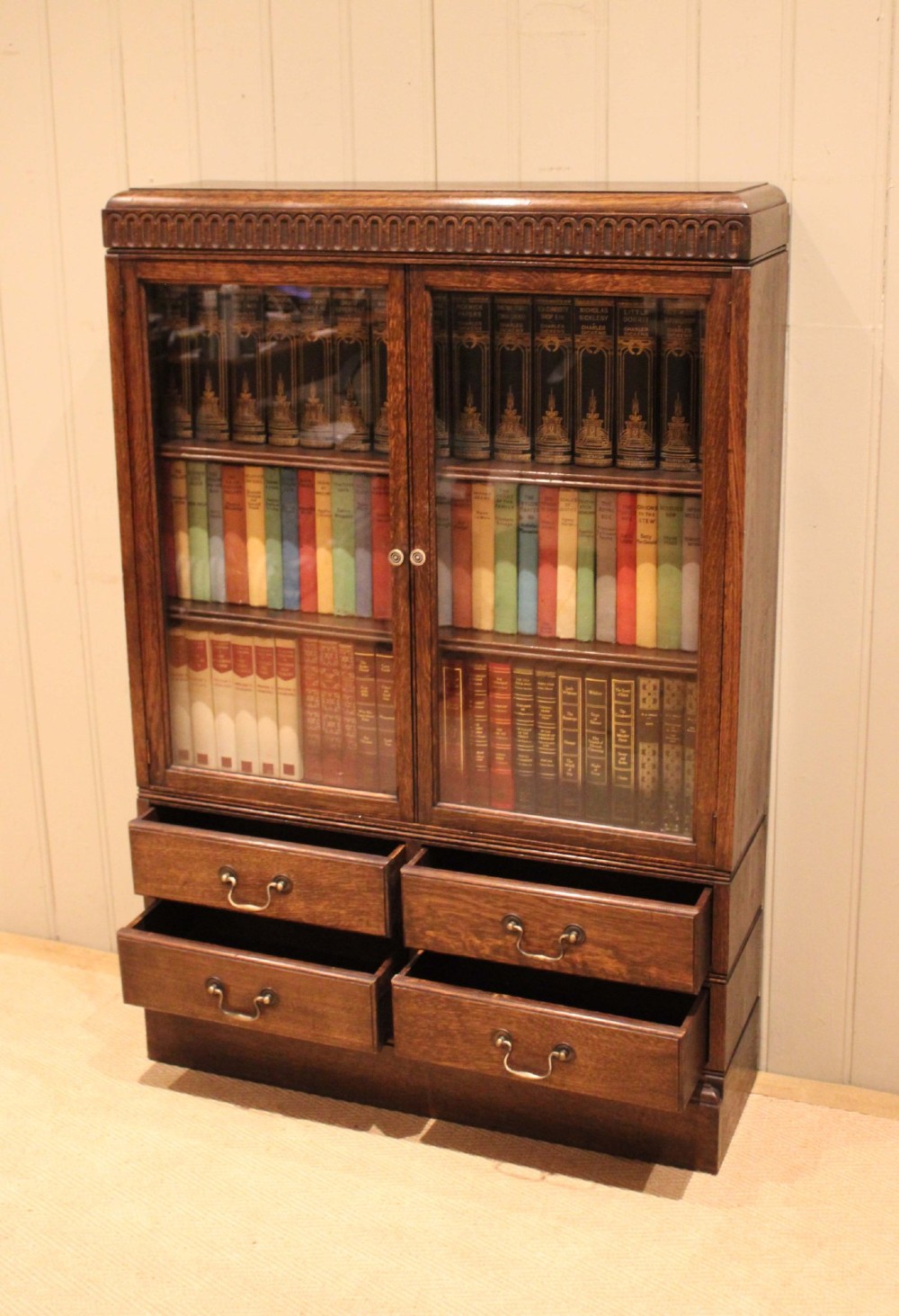 A medium brown oak glazed bookcase with two glass upper doors, carved egg-and-dart top moulding, and four drawers with brass handles. View III