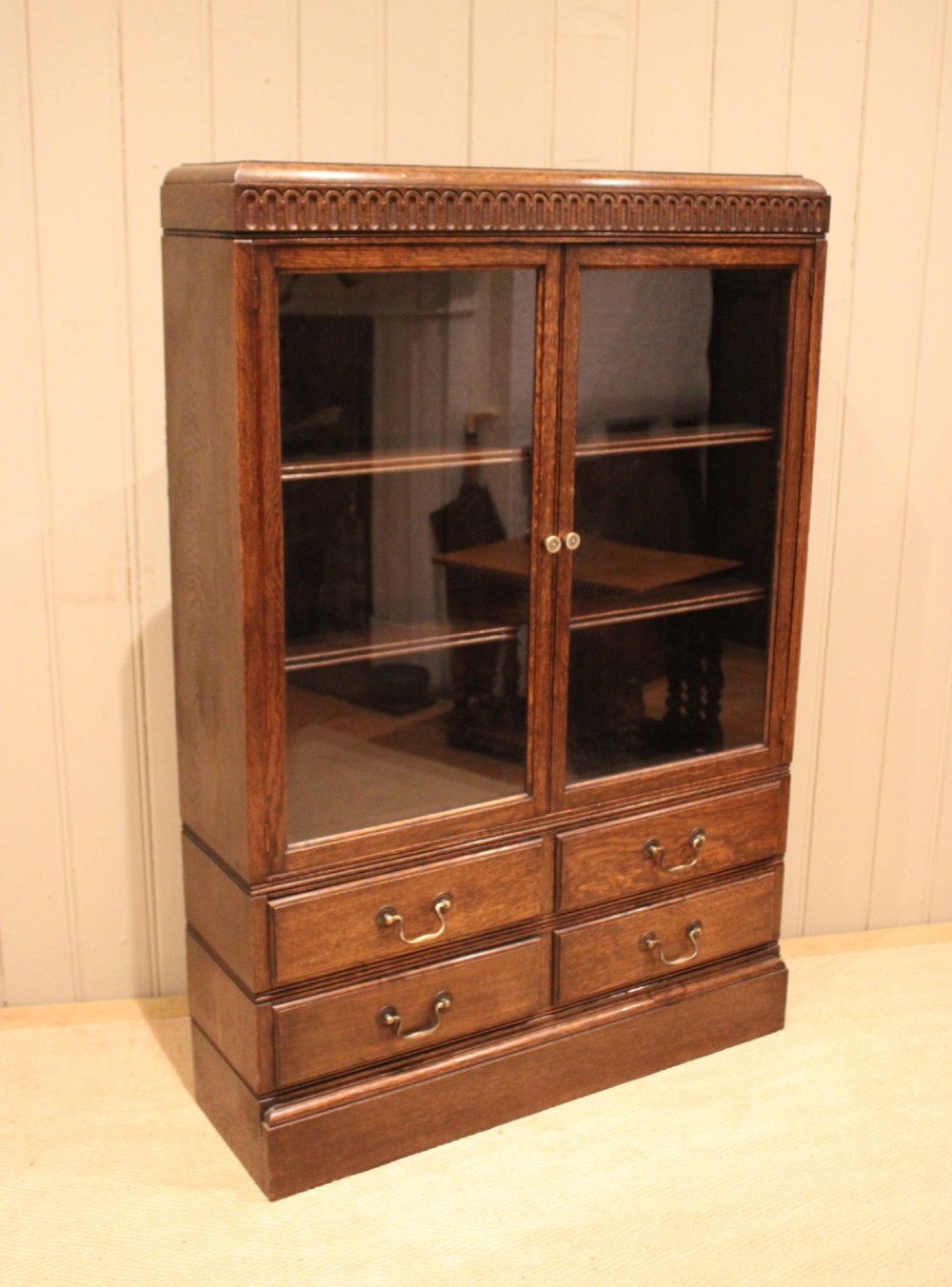 A medium brown oak glazed bookcase with two glass upper doors, carved egg-and-dart top moulding, and four drawers with brass handles. View IV