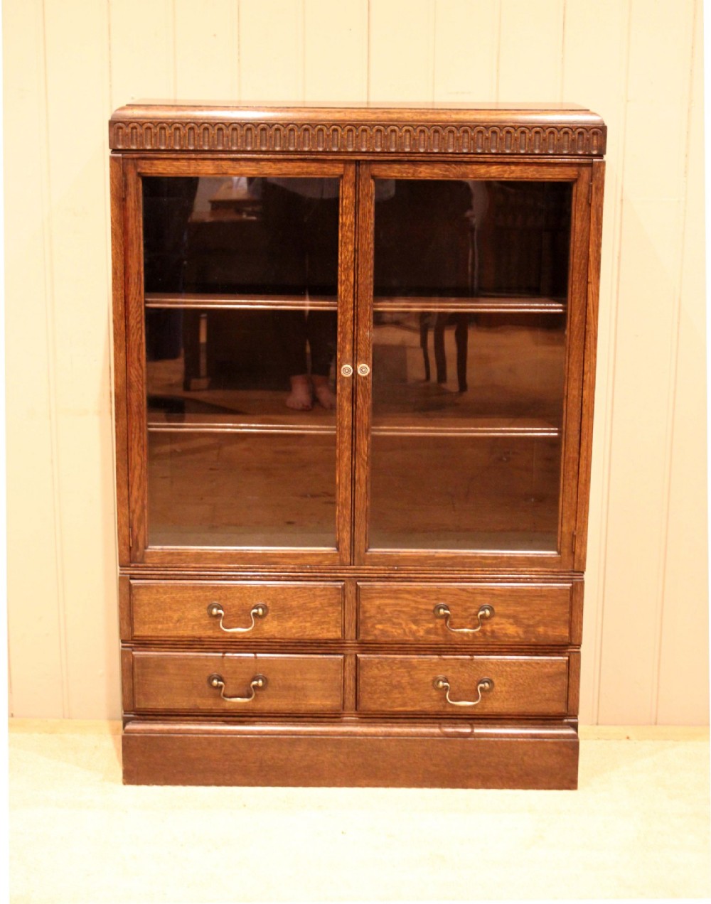 A medium brown oak glazed bookcase with two glass upper doors, carved egg-and-dart top moulding, and four drawers with brass handles. View VI