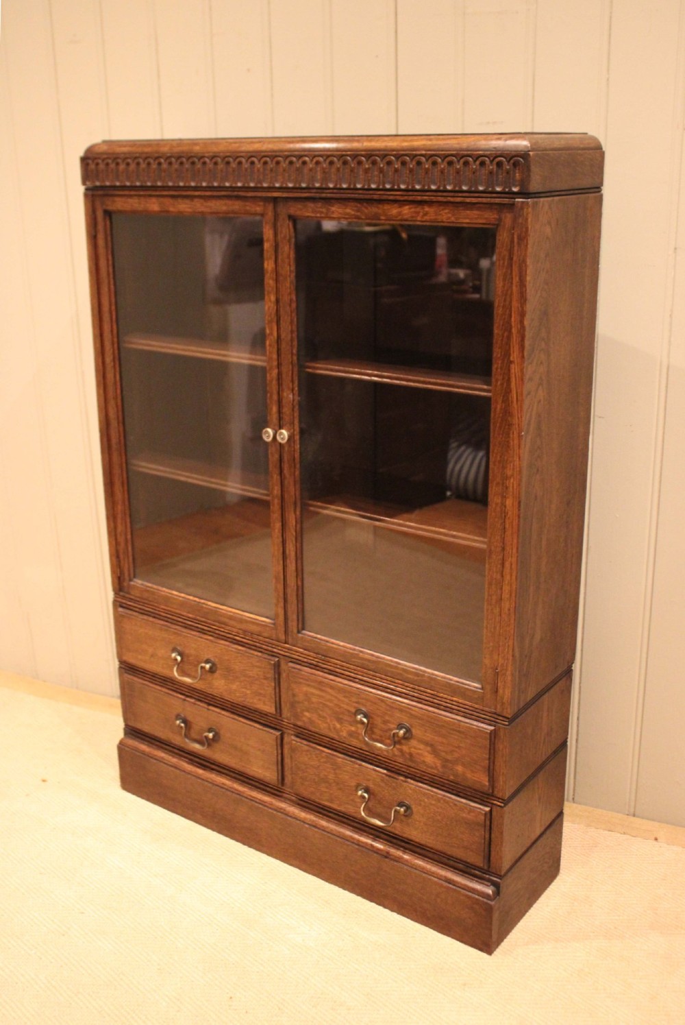 A medium brown oak glazed bookcase with two glass upper doors, carved egg-and-dart top moulding, and four drawers with brass handles. View VIII