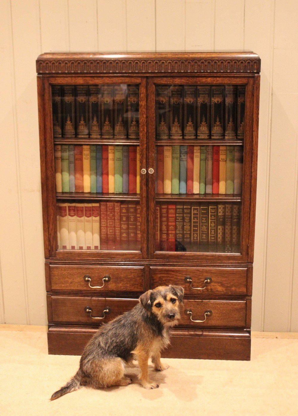 A medium brown oak glazed bookcase with two glass upper doors, carved egg-and-dart top moulding, and four drawers with brass handles. View IX