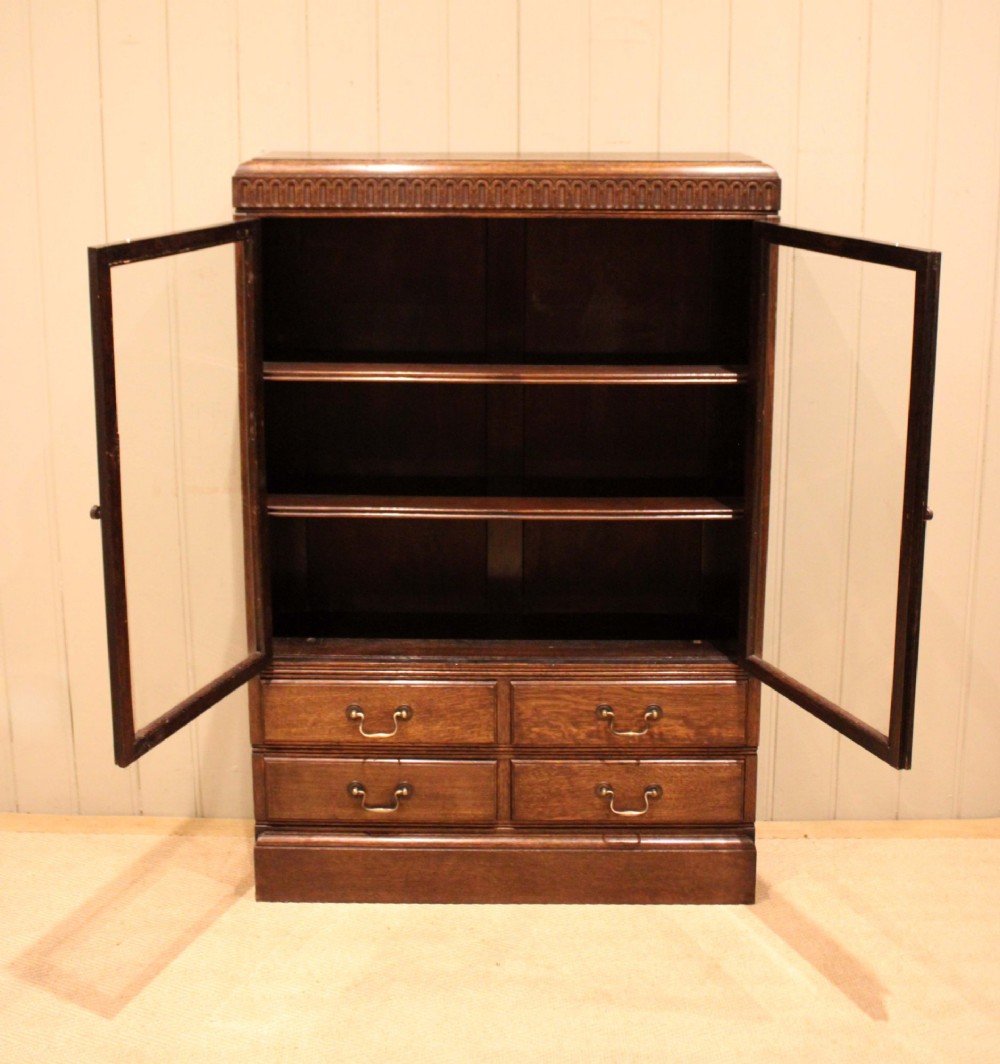 A medium brown oak glazed bookcase with two glass upper doors, carved egg-and-dart top moulding, and four drawers with brass handles. View X