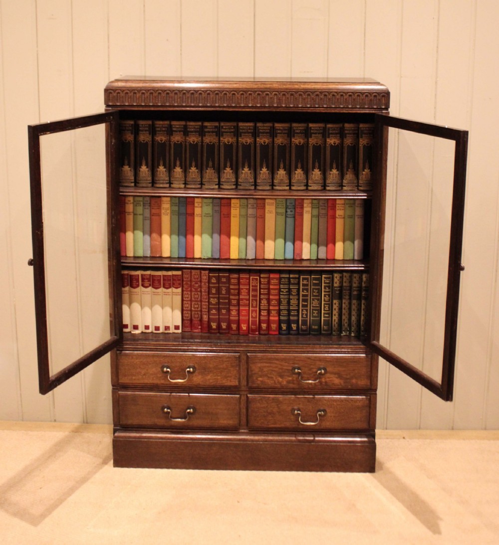 A medium brown oak glazed bookcase with two glass upper doors, carved egg-and-dart top moulding, and four drawers with brass handles. View XI