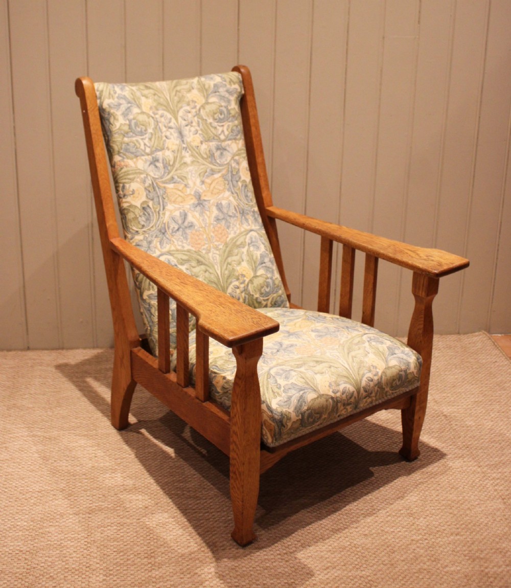 A solid oak Arts and Crafts style armchair featuring broad flat armrests and upholstery decorated with a botanical foliage pattern. View II