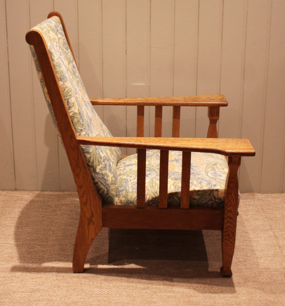 A solid oak Arts and Crafts style armchair featuring broad flat armrests and upholstery decorated with a botanical foliage pattern. View III