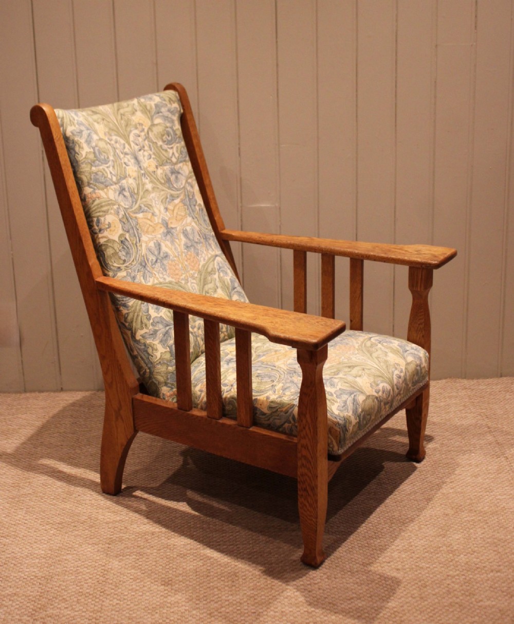 A solid oak Arts and Crafts style armchair featuring broad flat armrests and upholstery decorated with a botanical foliage pattern. View IV